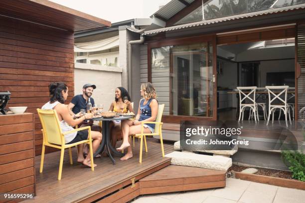 group of four young adults relaxing on patio outside house with food and drink - share house stock pictures, royalty-free photos & images