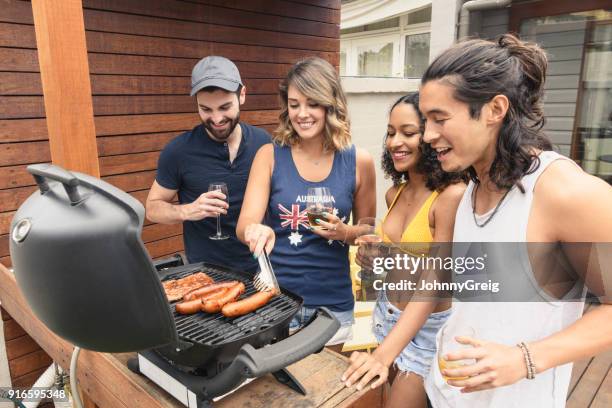 gruppe von vier jungen freunden kochen würstchen auf dem grill und lächelnd - bbq australia stock-fotos und bilder