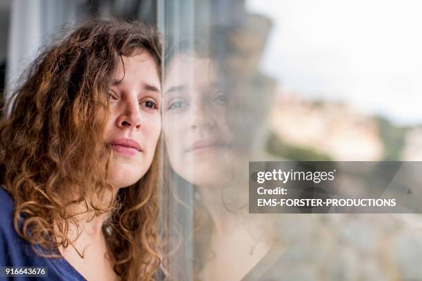 sad woman looking out of the window - hoffnungslosigkeit stock-fotos und bilder