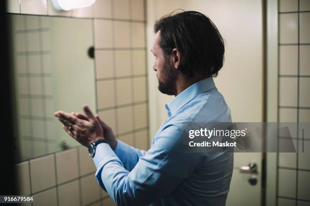 businessman rubbing hands while standing in front of mirror at bathroom - se frotter les mains photos et images de collection