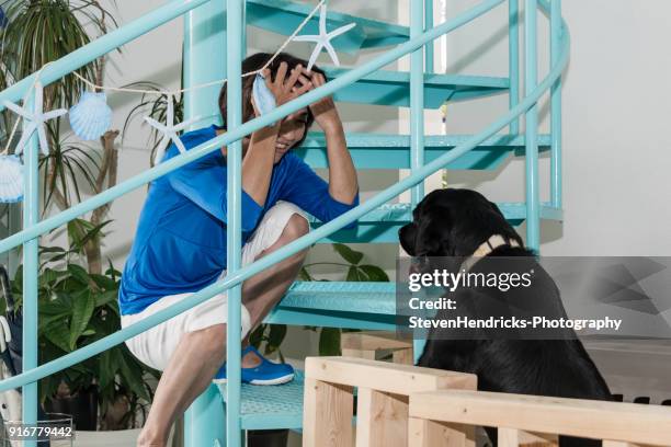 日本人女性をスクワットし、階段の隙間から彼女を見上げる黒犬をペット - 犬　人　カフェ ストックフォトと画像