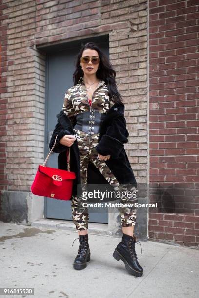 Guest is seen on the street attending Self-Portrait during New York Fashion Week wearing a camo jumpsuit with red bag and black fur coat on February...