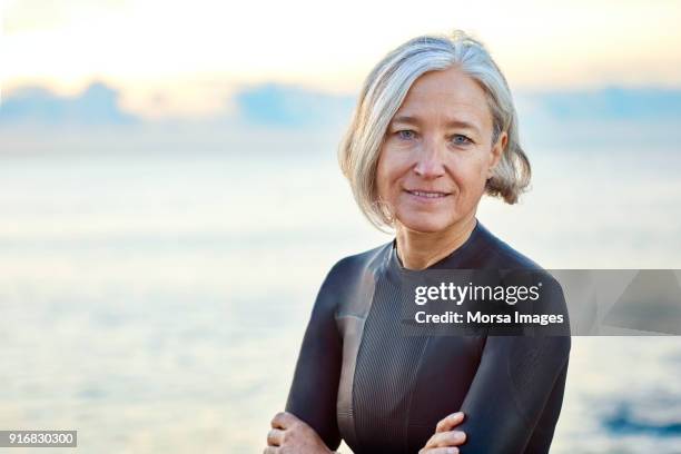 senior woman in wetsuit smiling at beach - senior woman short hair stock pictures, royalty-free photos & images