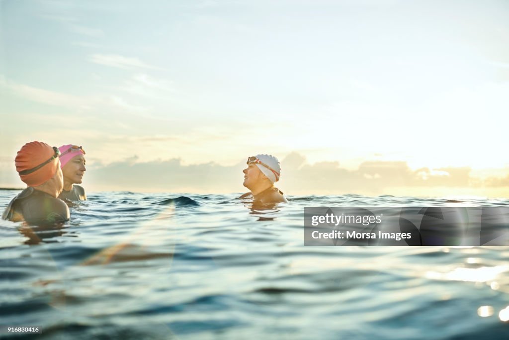 Women talking while swimming in sea during sunset