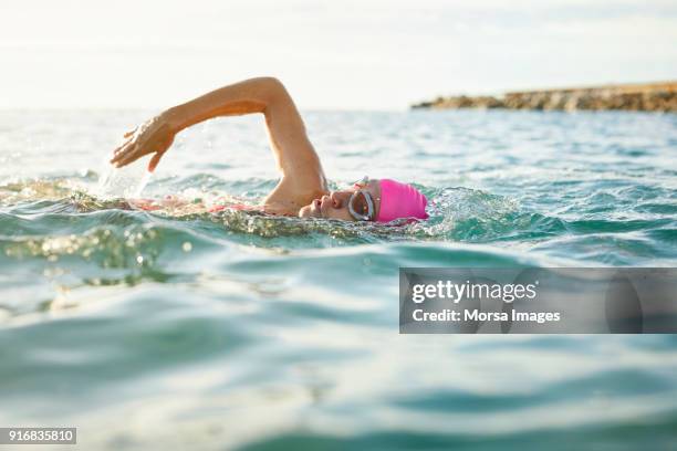entschlossenen senior frau im meer zu schwimmen - bademütze stock-fotos und bilder