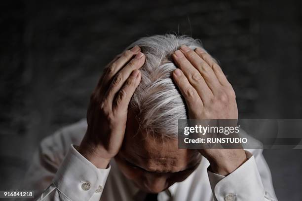 middle aged man holding head in pain and despair - wit haar stockfoto's en -beelden