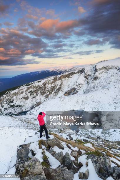 male photographer on top of a mountain taking pictures at snowy landscape and lake - confidence male landscape stock-fotos und bilder