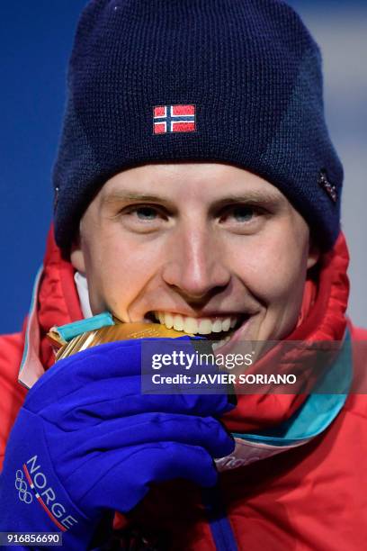 Norway's gold medallist Simen Hegstad Krueger bites his medal on the podium during the medal ceremony for the cross country 15km + 15km skiathlon at...