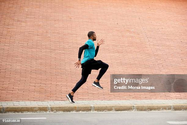 side view of dedicated athlete jogging by wall - running man profile stock pictures, royalty-free photos & images
