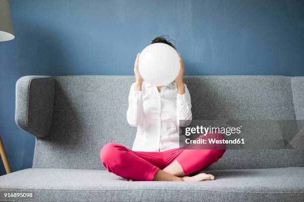 woman sitting on couch hiding her face behind a white sphere - boule de cristal photos et images de collection