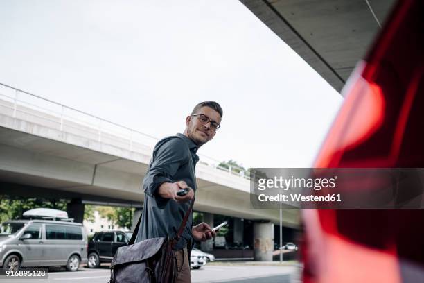 young businessman using remote control key of car - elektro auto stock-fotos und bilder
