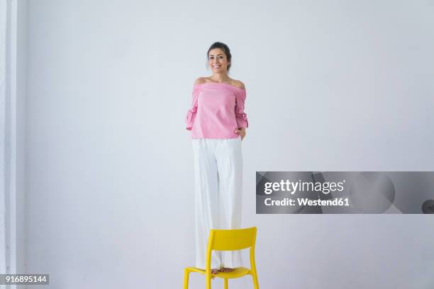 portrait of laughing woman standing on yellow chair - standing on chair stockfoto's en -beelden