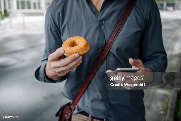 hands of businessman holding doughnut and smartphone, partial view - eating donuts foto e immagini stock