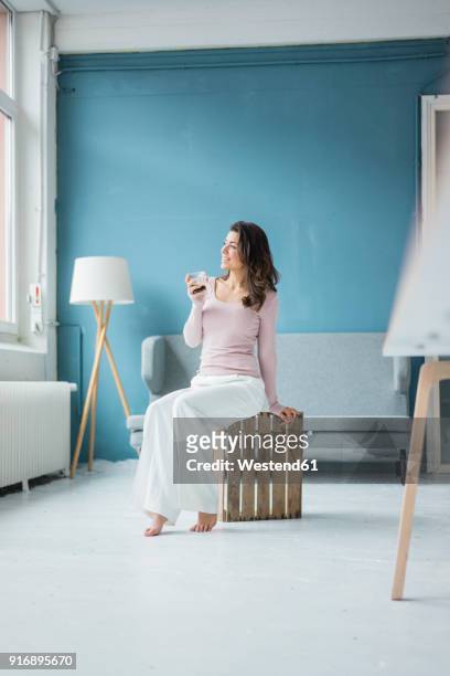 young woman relaxing with glass of coffee in a loft looking out of window - sitting drinking coffee man stock-fotos und bilder