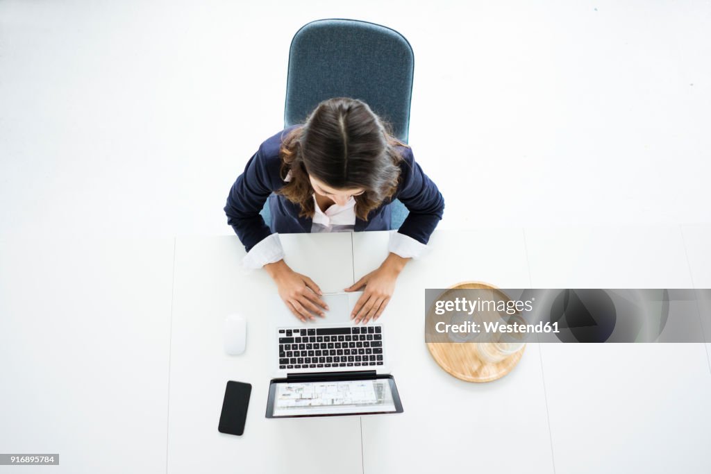 Businesswoman sitting at desk in the office working on laptop, top view