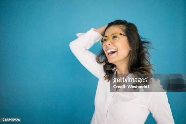 portrait of laughing woman wearing glasses in front of blue background - eccitazione foto e immagini stock