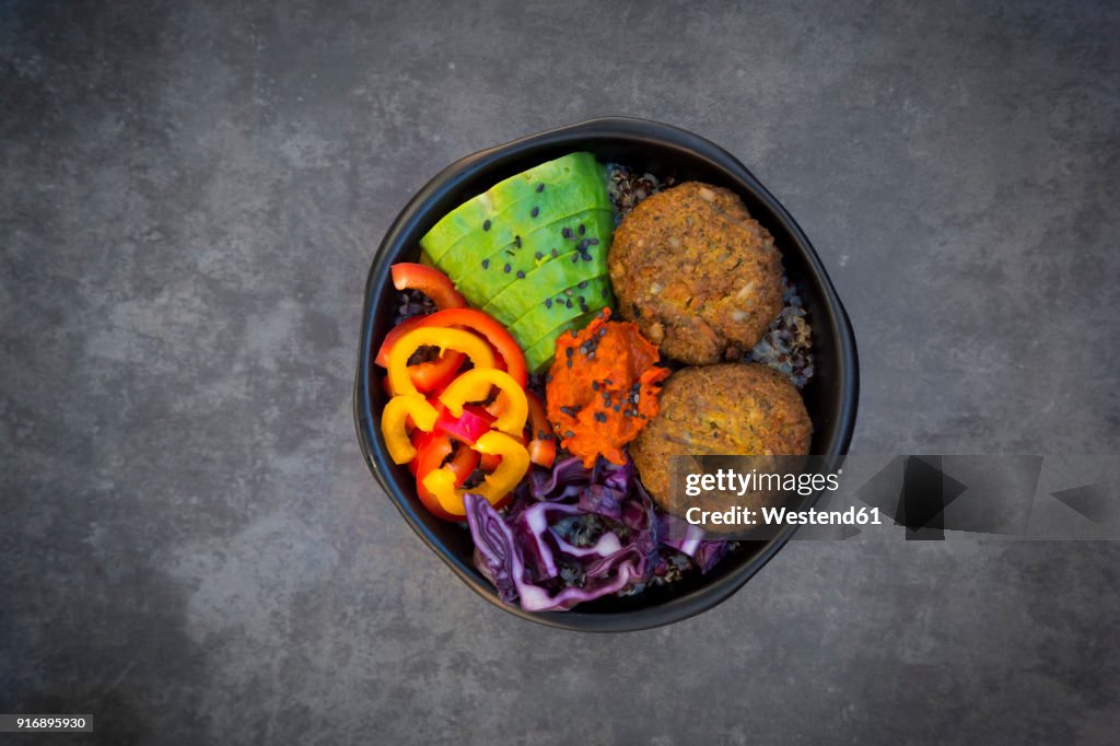 Lunch bowl of quinoa, red cabbage, bell pepper, avocado, quinoa fritters, ajvar and black sesame