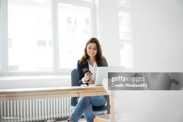 businesswoman sitting at desk in the office working on laptop - blank smartphone stock pictures, royalty-free photos & images