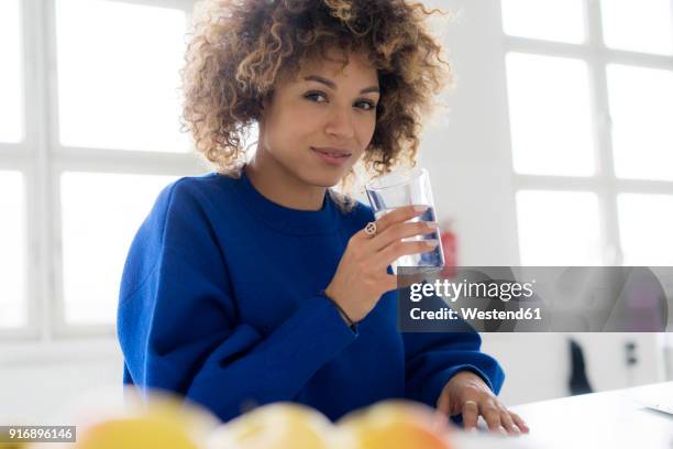 portrait of smiling young woman drinking glass of water at table - blue sweater stockfoto's en -beelden