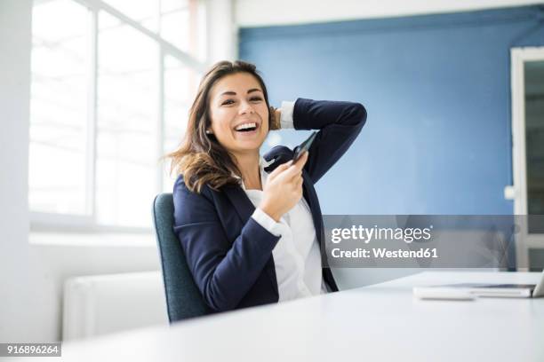 portrait of laughing businesswoman with cell phone sitting at desk in the office - input device stock-fotos und bilder