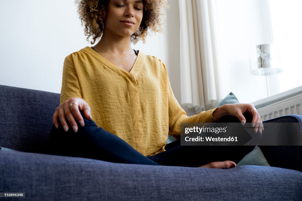 Young woman sitting on couch at home meditating