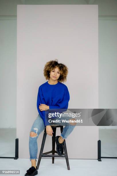 portrait of serious woman wearing blue pullover sitting on stool - sgabello foto e immagini stock