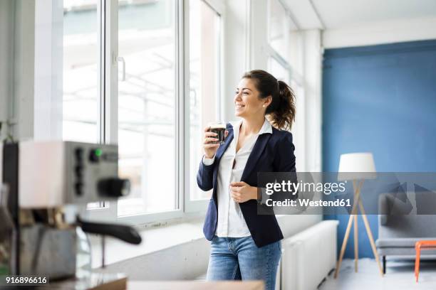 happy businesswoman with glass of coffee in a loft looking out of window - leisure work coffee happy stockfoto's en -beelden