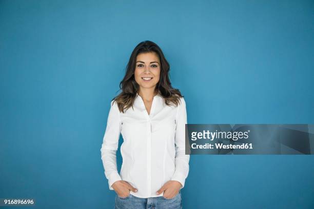 portrait of smiling woman standing in front of blue wall - blusa azul imagens e fotografias de stock