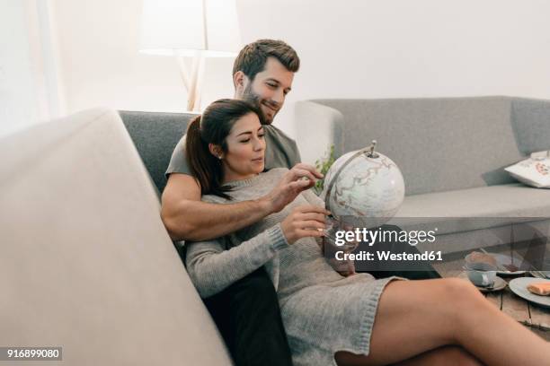 couple relaxing on couch at home looking at globe - world bank stockfoto's en -beelden