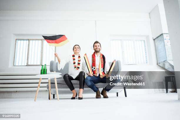 happy german football fan couple sitting on couch watching tv - soccer scarf stock pictures, royalty-free photos & images