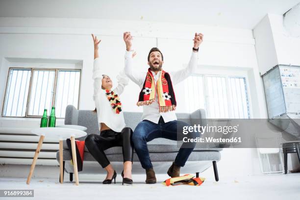 excited german football fans cheering on couch - supporter scarf stock pictures, royalty-free photos & images