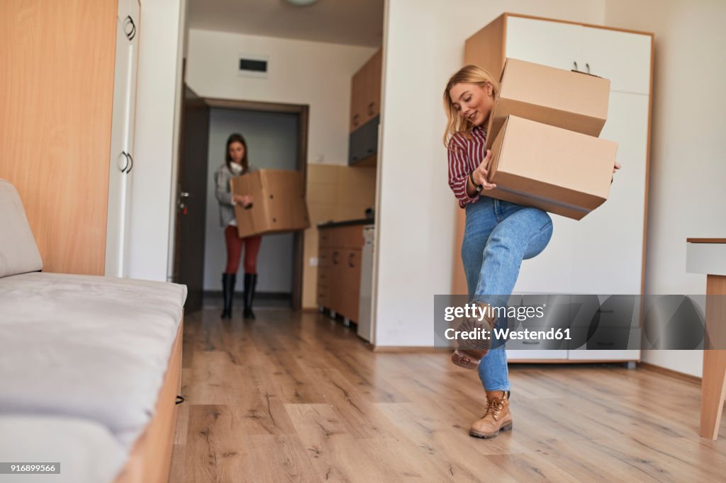 Two young women carrying cardboard boxes into a room