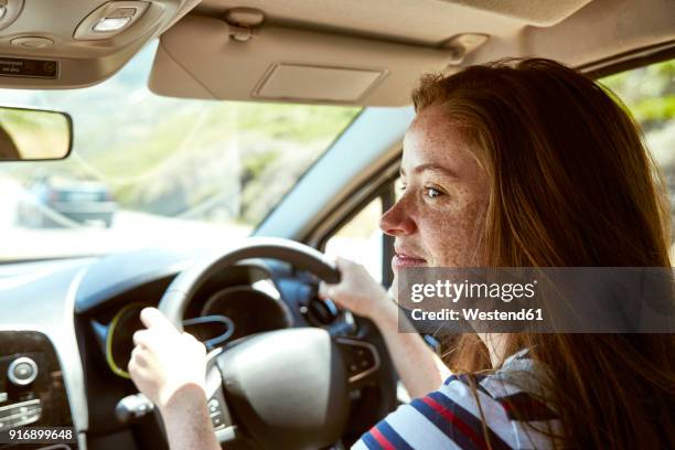 smiling young woman with freckles driving car looking sideways - woman driving fotografías e imágenes de stock