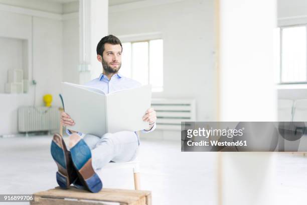 businessman sitting in empty loft office holdig large folder - grande tablée photos et images de collection