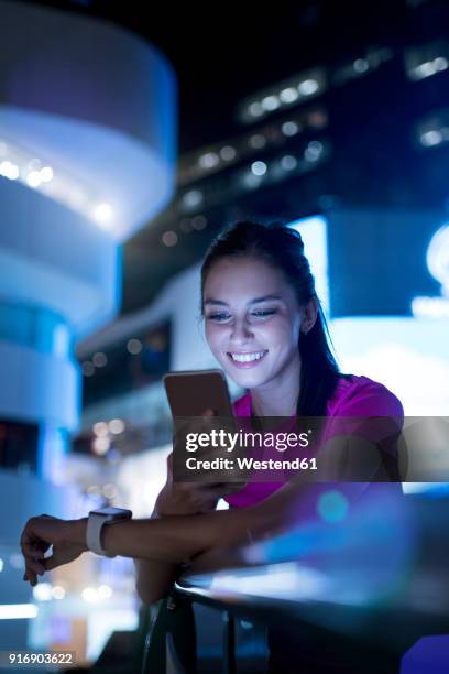 young woman in pink sportshirt checking her smartphone in city at night - instant messaging photos et images de collection