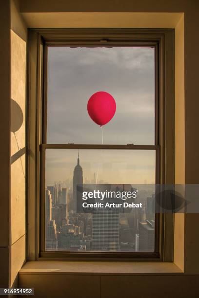 poetic picture of red balloon flying in the manhattan skyline with picture taken from inside the window. - empire state building red stock pictures, royalty-free photos & images