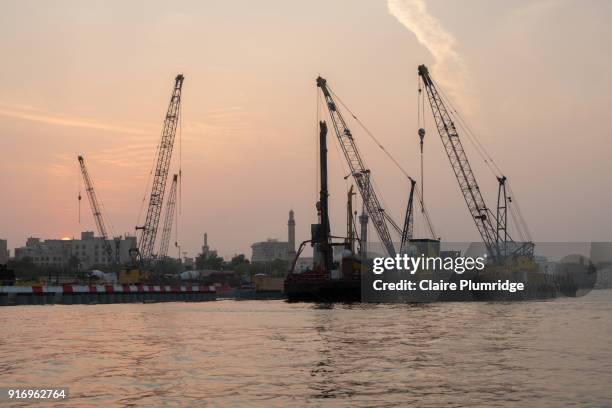 cranes loading and unloading from cargo ships, in dubai creek, united arab emirates. taken at dusk. - claire plumridge fotografías e imágenes de stock