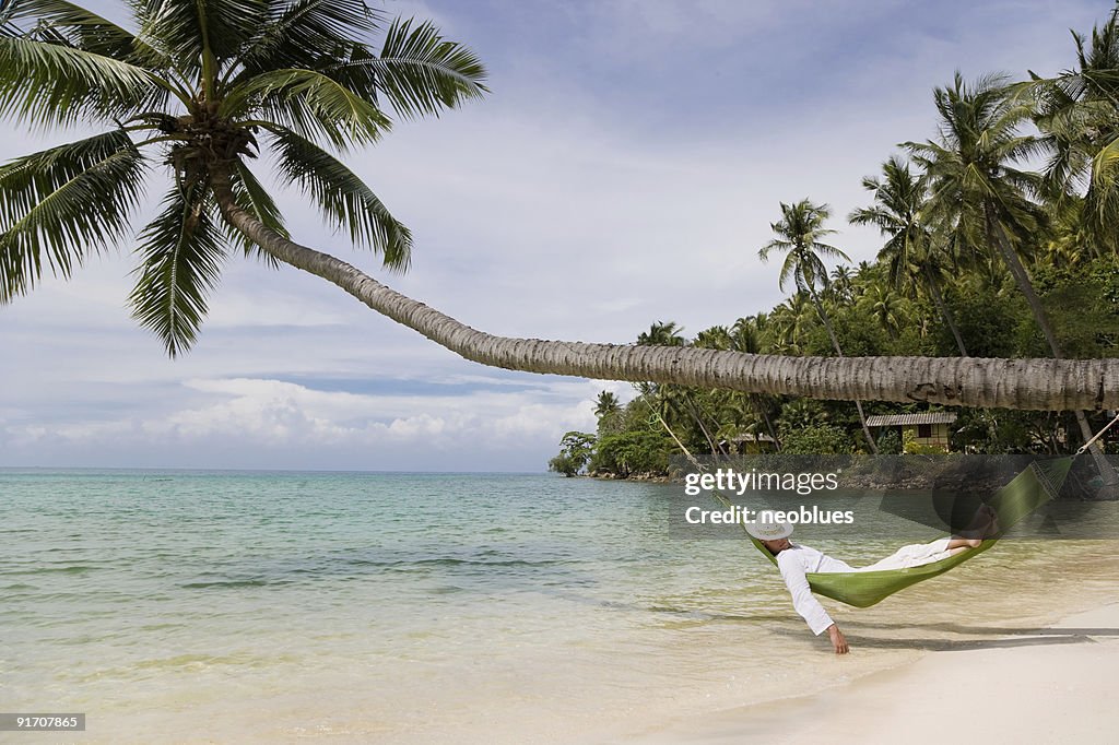 Man lying on green beach hammock hanging from palm tree