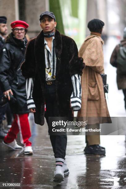 Guest wears a cap, a choker, a fur coat, a striped shirt, pants, white sneakers, under the rain, outside Paul Smith, during Paris Fashion Week -...