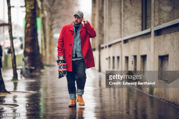 Guest wears a cap, a red jacket, orange shoes, black pants, a colored clutch, under the rain, outside Paul Smith, during Paris Fashion Week -...