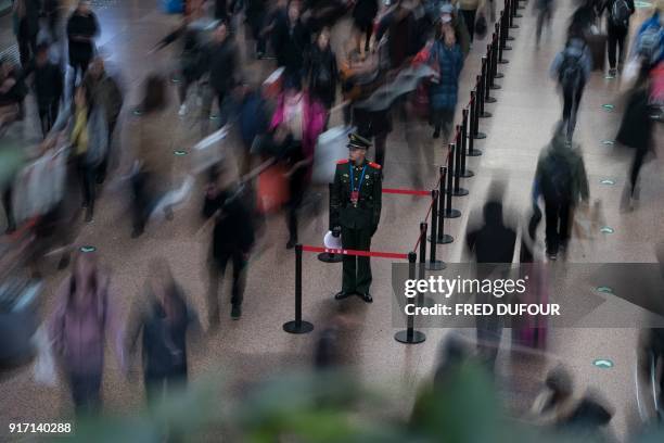 This photo taken on February 10, 2018 shows a Chinese soldier standing in the main hall while travellers rush before boarding trains at the West...