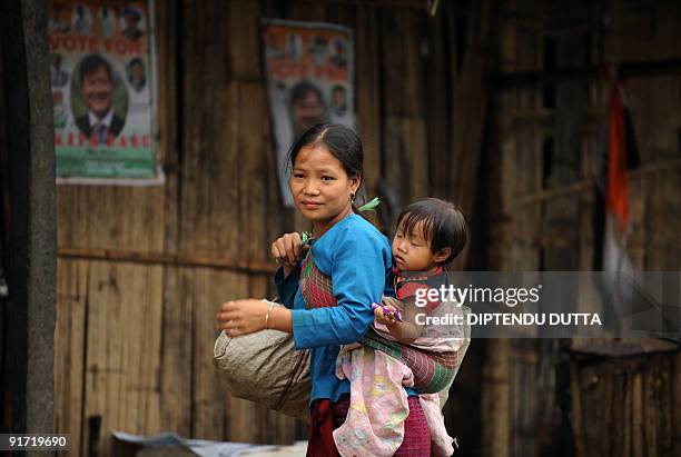 An Indian tribal woman carrying a child walks past a poster of Congress party State Assembly candidate Kipa Babu in Itanagar, capital of Arunachal...