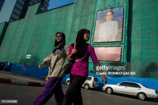Two Muslim women pass a huge portrait of Myanmar's de facto leader Aung San Suu Kyi displayed on a building construction site overlooking...