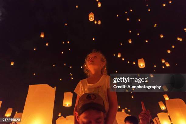 the tourist girl sit on father's neck looking the lanterns were floating in the sky. - yi peng stock-fotos und bilder