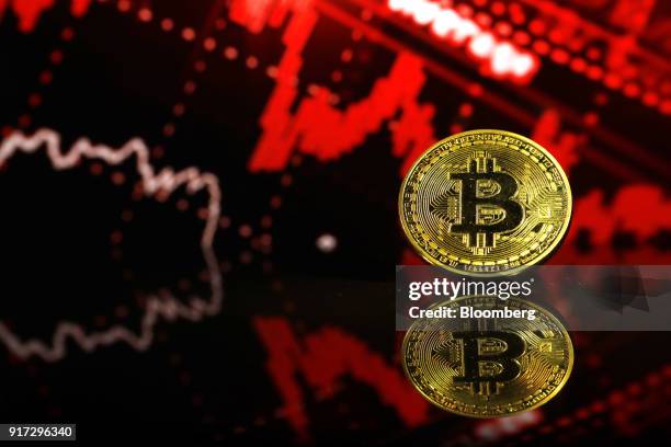 Coin representing Bitcoin cryptocurrency sits reflected on a polished surface and photographed against a photo illustration of electronic data...