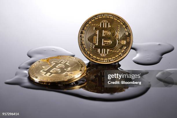 Two coins representing Bitcoin cryptocurrency are reflected on a polished surface as they sit in a pool of translucent liquid in this arranged...