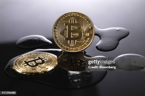 Two coins representing Bitcoin cryptocurrency are reflected on a polished surface as they sit in a pool of translucent liquid in this arranged...