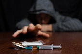 Addict at the table pulls his hand to the syringe with the dose