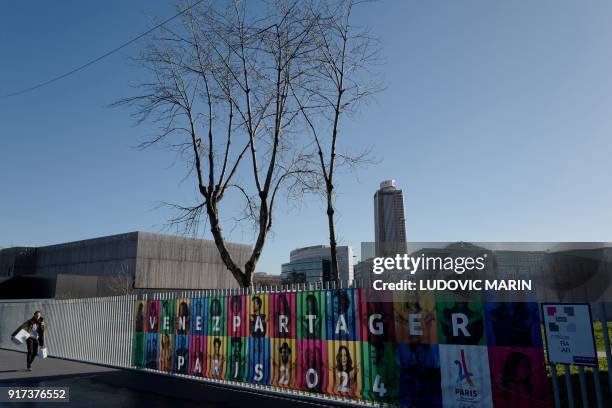 Man walks in a street past a banner promoting the 2024 Olympic Games hosted in France, on Febuary 12, 2018 in Saint-Denis, northern suburbs of Paris....