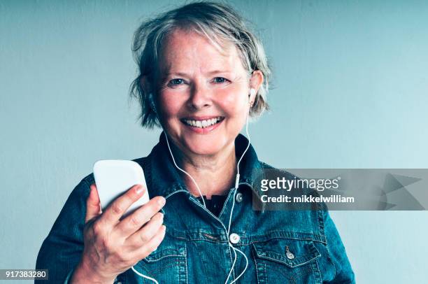 senior women listens to podcast through headset connected to her mobile phone - free pics com stock pictures, royalty-free photos & images